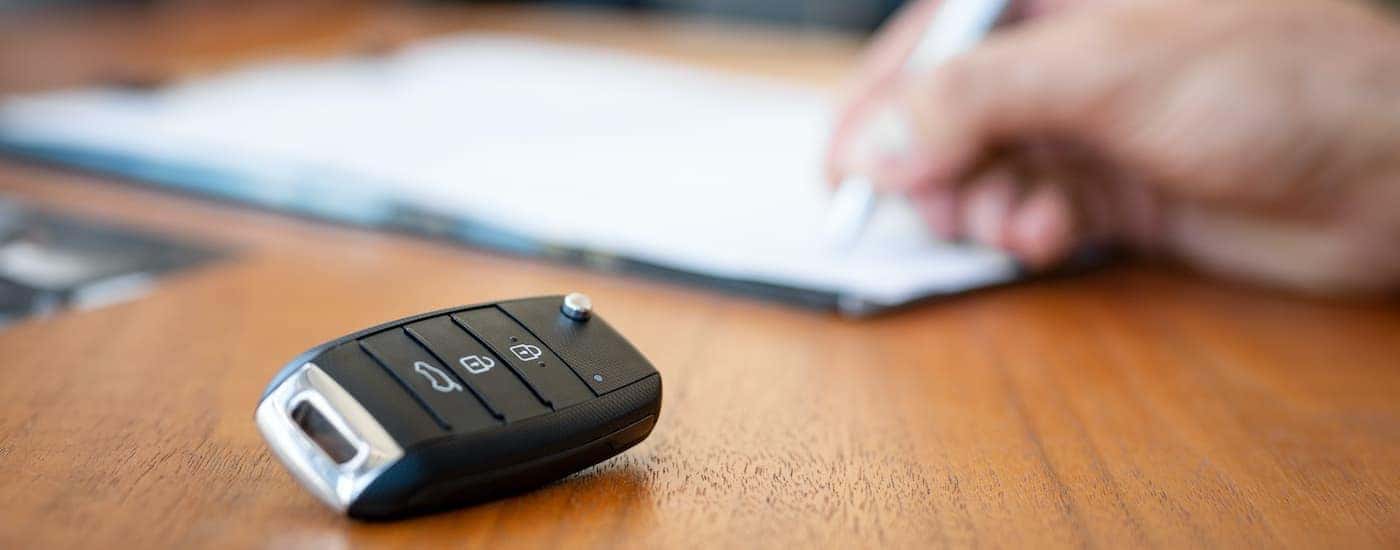 A car key is shown next to a person signing paperwork after deciding to sell your car.