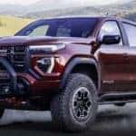 A red 2023 GMC Canyon is shown driving on a dirt road.