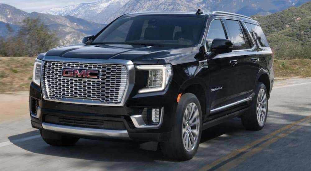 A black 2023 GMC Yukon is shown from the front driving away from a car lot near you.