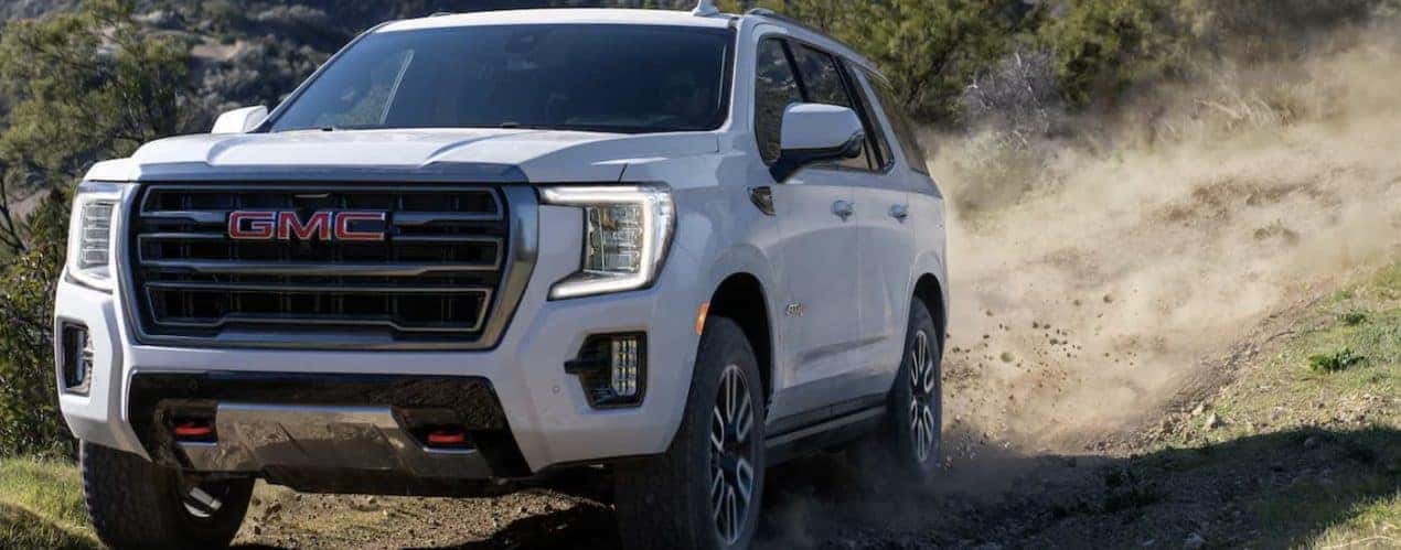 A white 2023 GMC Yukon AT4 is shown driving on a dirt road.