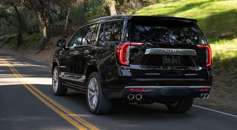 A black 2023 GMC Yukon Denali Ultimate is shown from the rear driving on a forest road.
