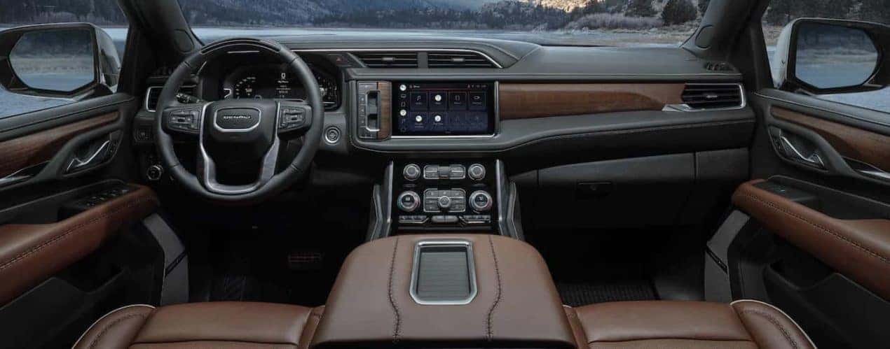 The black and brown interior of a 2023 GMC Yukon shows the steering wheel and infotainment screen.