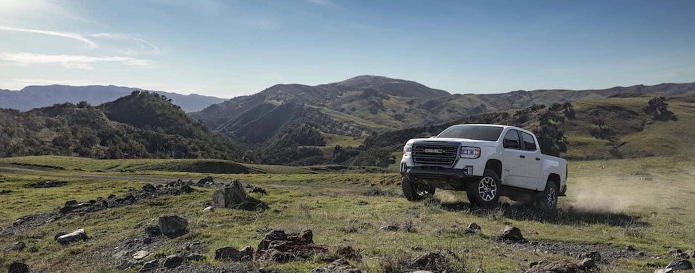 A white 2022 GMC Canyon AT4 is shown driving in an open plain after leaving a dealer that had lifted trucks for sale.