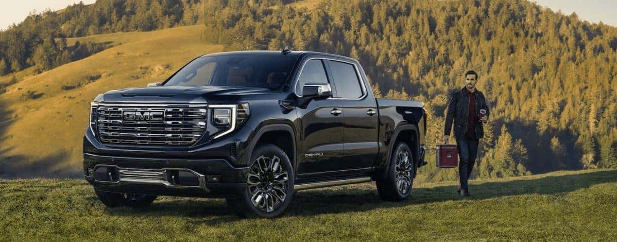 A black 2023 GMC Sierra 1500 Denali is shown parked on a grassy hill overlooking a mountain.
