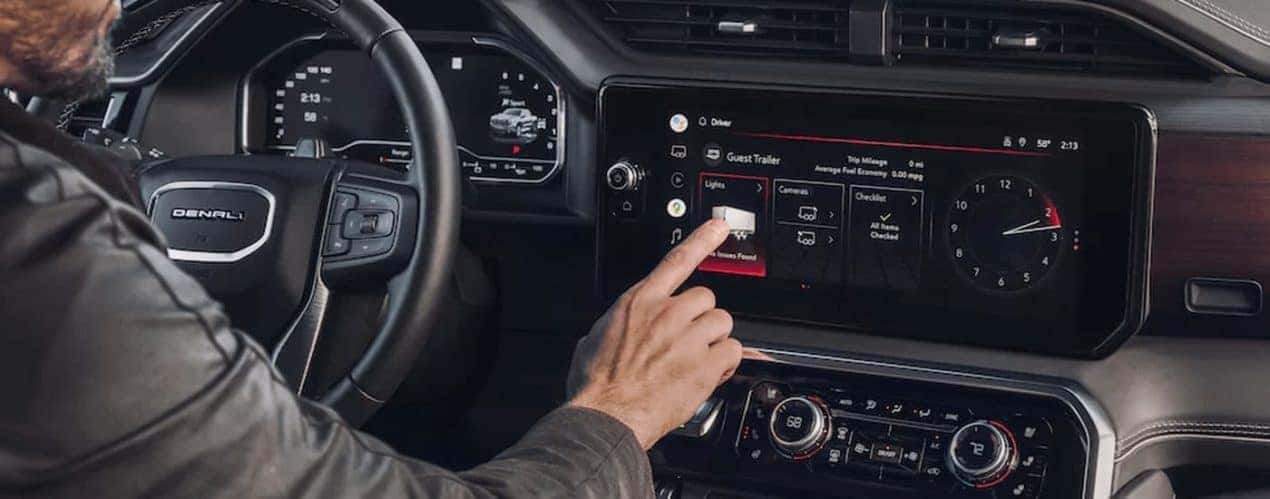 A person is shown using the infotainment screen in a 2023 GMC Sierra 1500 during a 2023 GMC Sierra 1500 vs 2023 Ford F-150 comparison.
