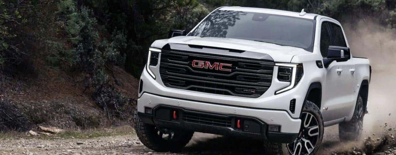 A white 2023 GMC Sierra 1500 AT4 is shown driving on a dirt road.