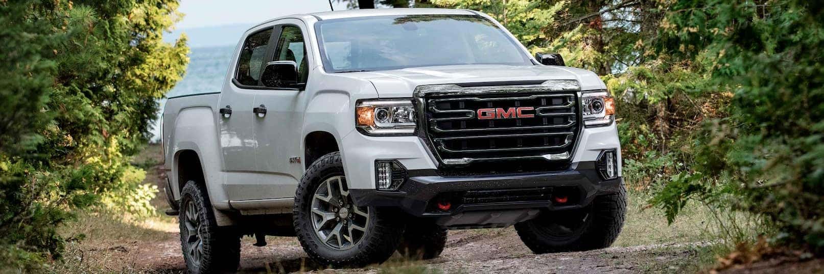 A white 2022 GMC Canyon AT4 is shown parked on a dirt road lined with trees.