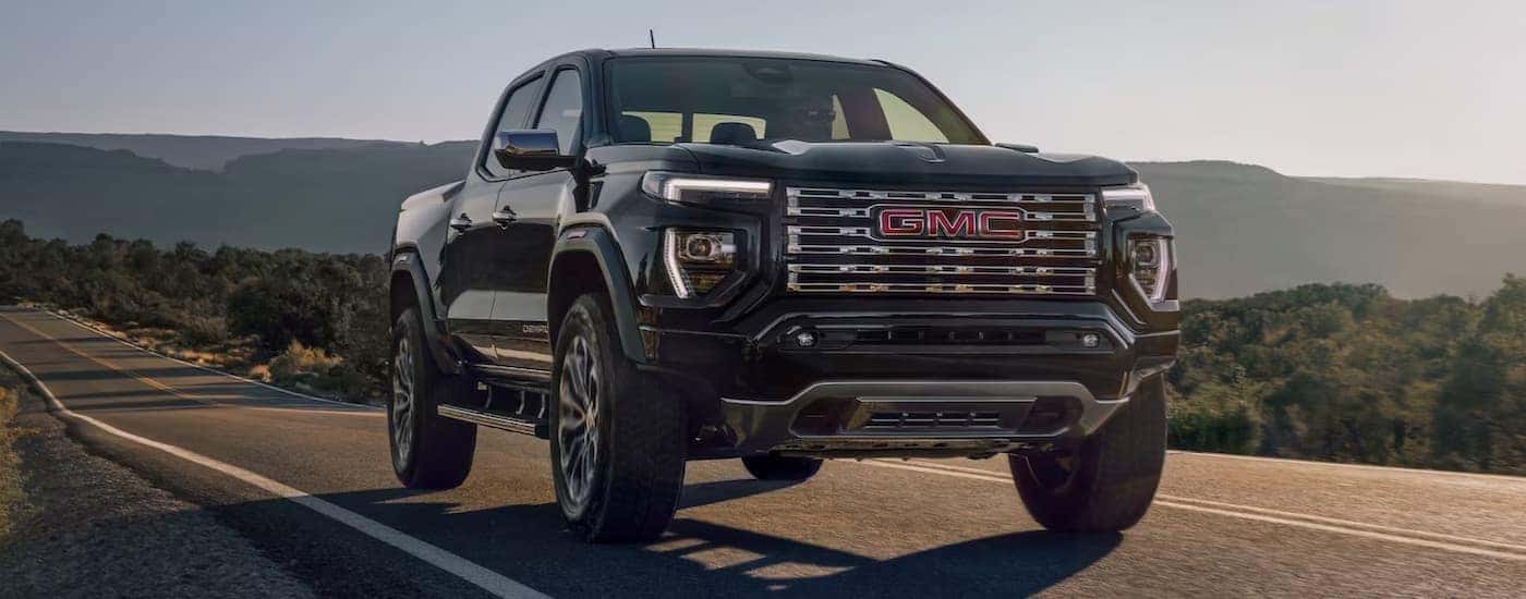 A black 2023 GMC Canyon Denali is shown driving on an open highway.