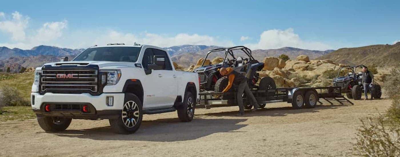 A white 2020 GMC Sierra 2500HD AT4 is shown from the front at an angle while towing a UTV.