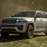 2026 Jeep Grand Cherokee SUV parked on a grassy field, showcasing its updated front grille, LED headlights, and modern exterior design.