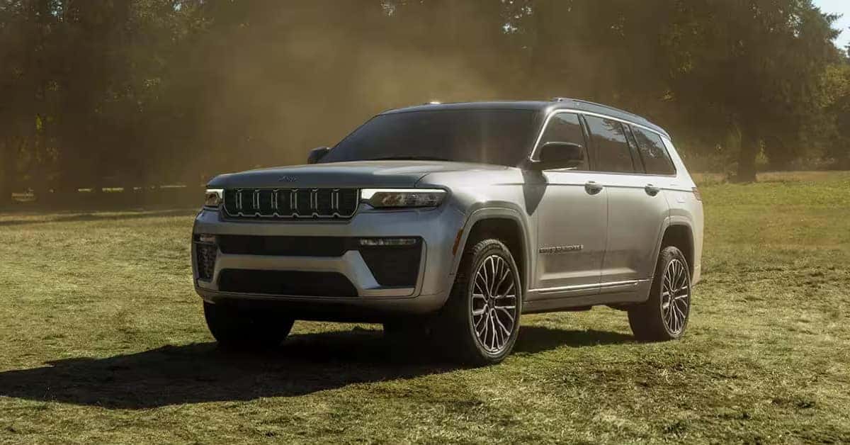 2026 Jeep Grand Cherokee SUV parked on a grassy field, showcasing its updated front grille, LED headlights, and modern exterior design.