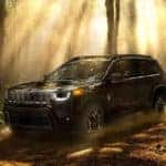 2026 Jeep Cherokee driving on a forest trail surrounded by trees and sunlight.