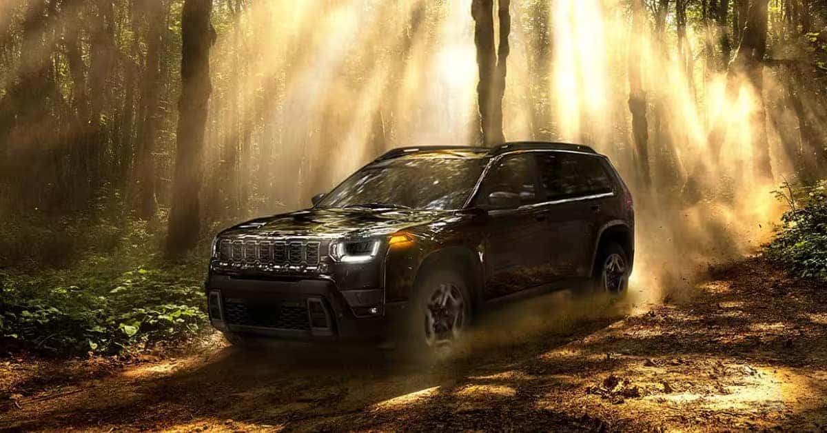 2026 Jeep Cherokee driving on a forest trail surrounded by trees and sunlight.