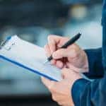 Auto mechanic holding a clipboard and assessing services.