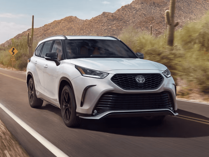 A white Toyota Highlander drives down a desert highway.