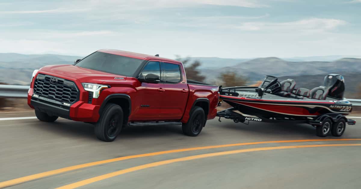 A red Toyota Tundra hauling a boat behind it on the road.